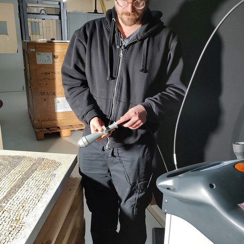11 Francesco Wiesner zeigt die Arbeit am Mosaik aus dem «Palazzo» von Insula 41/47. Dieses wurde 1972 geborgen, mit Zweikomponentenkleber geklebt und an der Oberfläche mit Wachs behandelt. Vergrösserte Ansicht