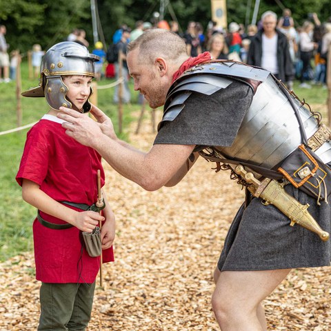 Ein-Legionär-hilft-beim-Justieren-des-Legionärshelms.jpg. Vergrösserte Ansicht
